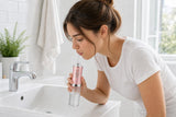 Mujer usando el irrigador Oravia inclinada sobre el lavabo, con los labios cerrados alrededor de la boquilla
